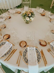 Vista cenital de mesa redonda decorada para banquete de boda con bajo platos de cerámica azul y dorada y centro floral silvestre. Decoración de mesa redonda para banquete de boda mediterráneo
